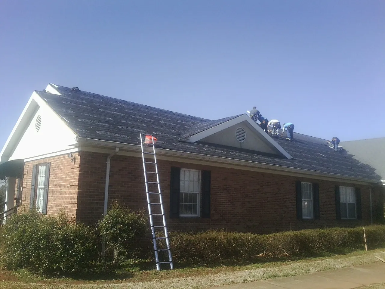 Crew tearing shingles off a brick ranch roof with a ladder set — Emergency Roof Repair work by our crew in Vincent