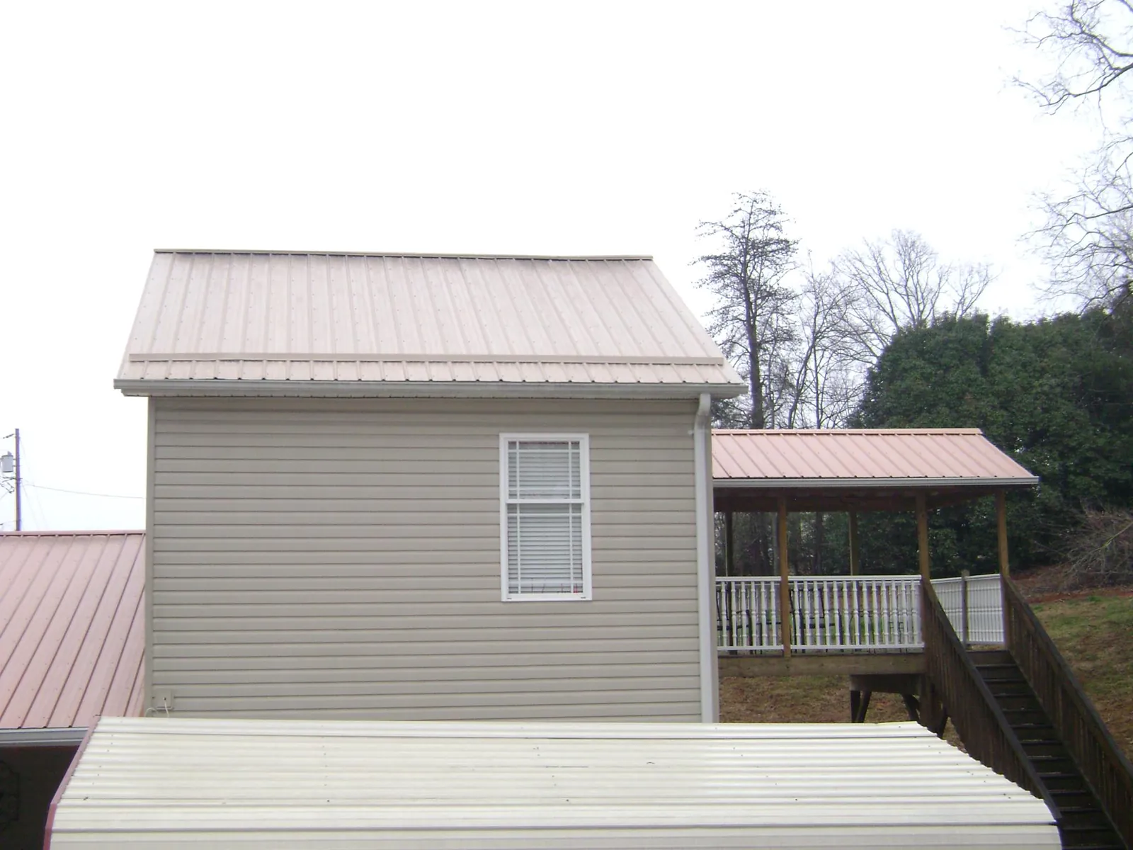 Tan metal roofs on a two story addition and attached porch, from a Roof Replacement job in Vincent